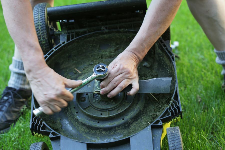 Man using a tool to tighten the nut of the mower blade